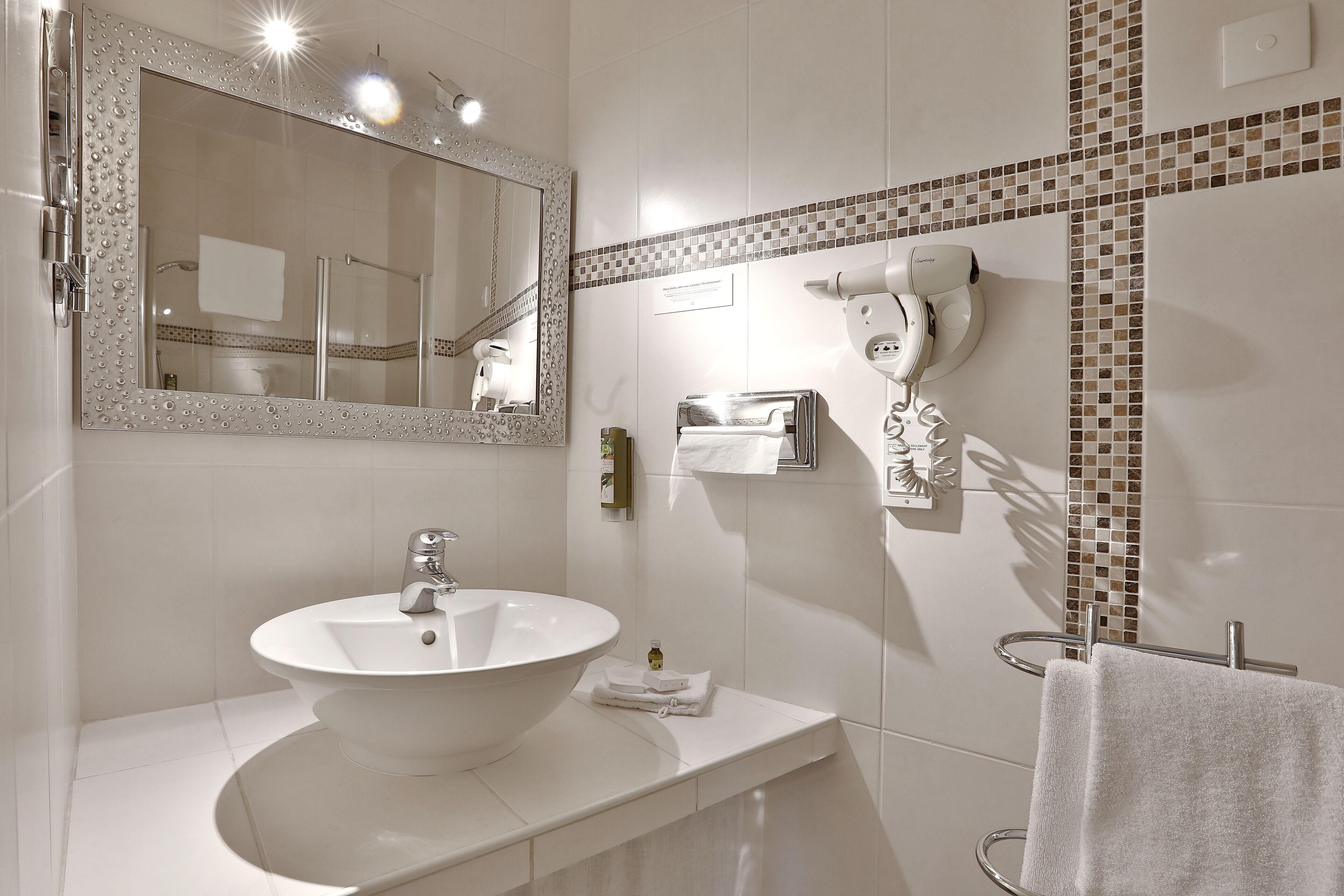 A modern bathroom with a large oval sink, a mirror with a decorative frame, a hairdryer, and a towel rack.