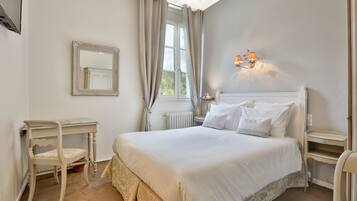 A bedroom with a large bed, a bedside table, a chair, a mirror, and a window with curtains.