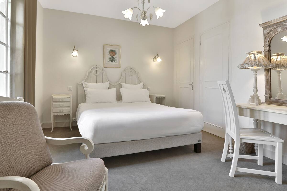Une chambre à coucher avec un grand lit, deux tables de chevet, une chaise, un bureau et un miroir.