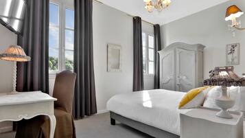 A hotel room with a bed, a desk, a chair, a wardrobe, and a chandelier.