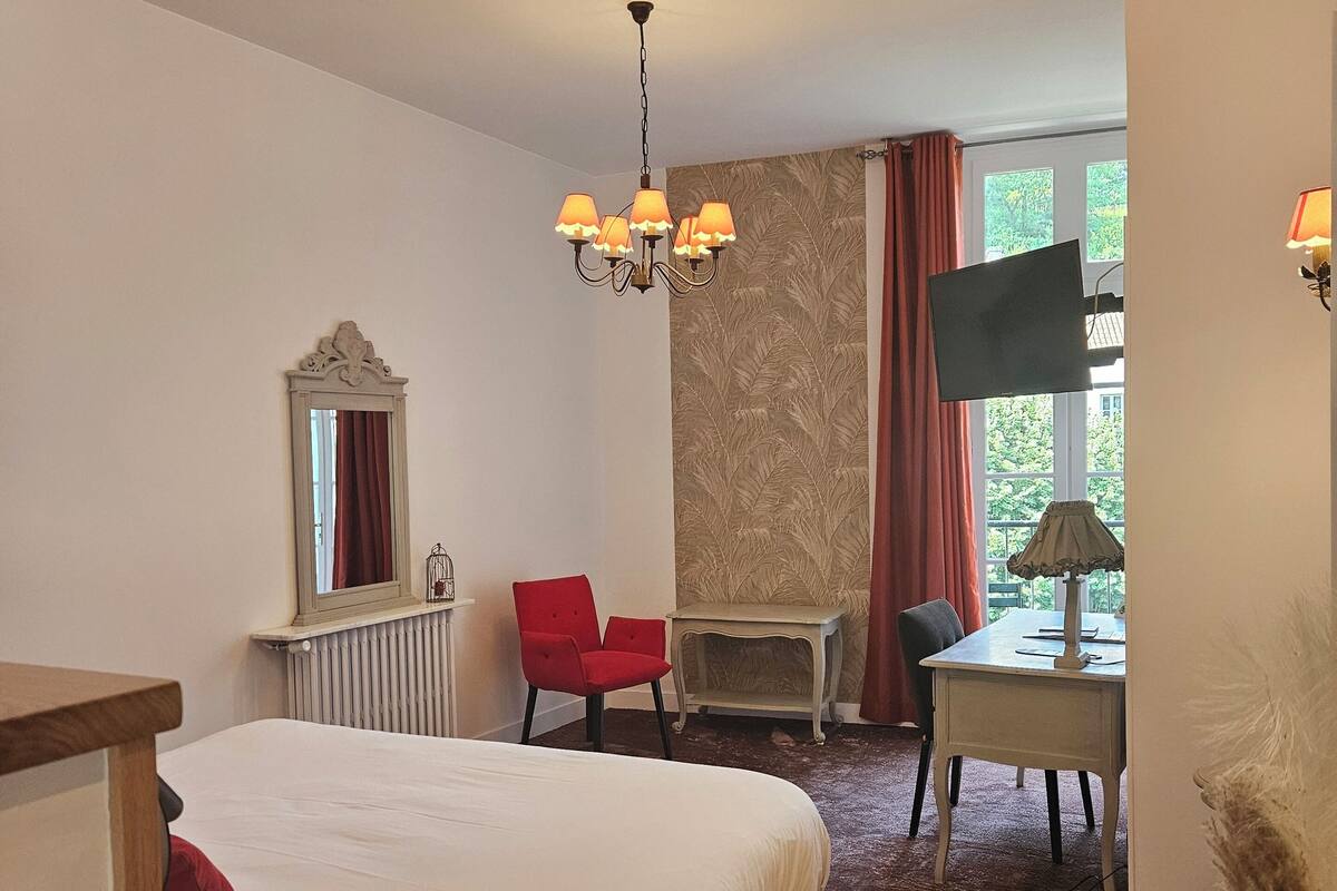 Une chambre d’hôtel avec un grand lit, un bureau, une chaise, une télévision et un lustre.