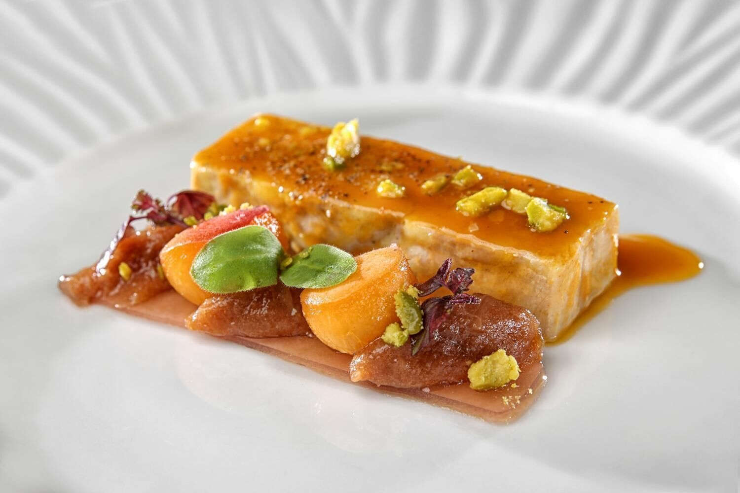 A dessert plate with a rectangular piece of caramel and various fruits and nuts.