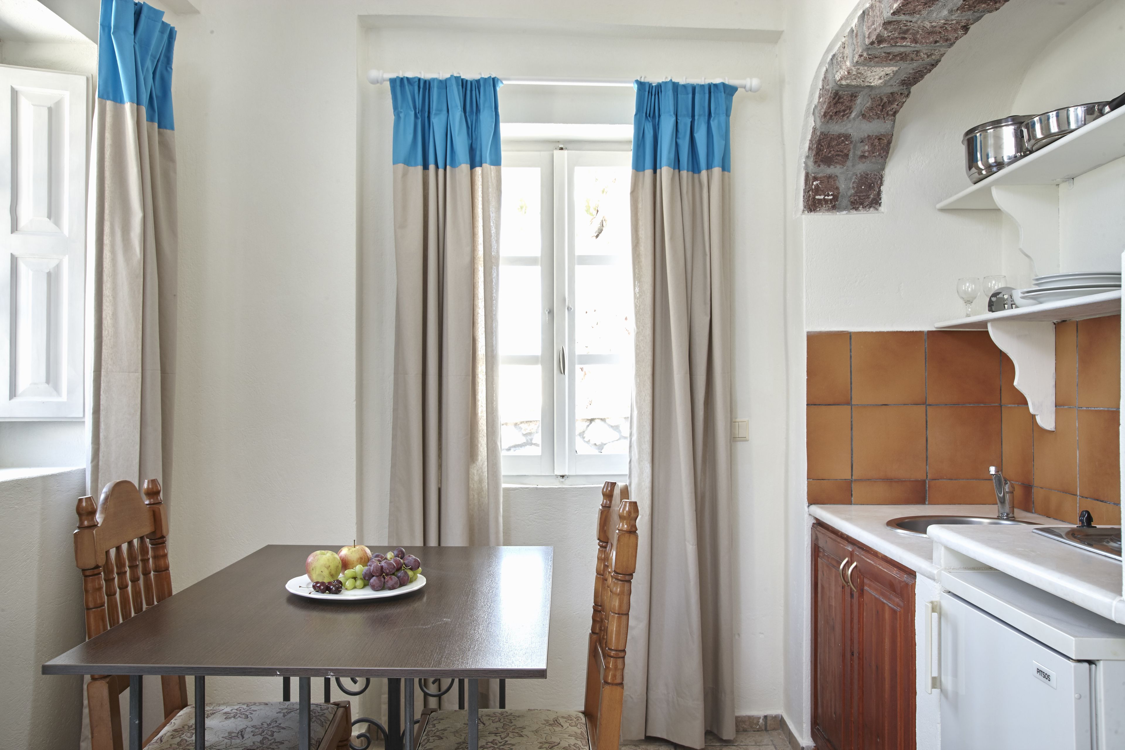 A dining area with a table set for two, a fruit plate, and a kitchen with a sink and cabinets.