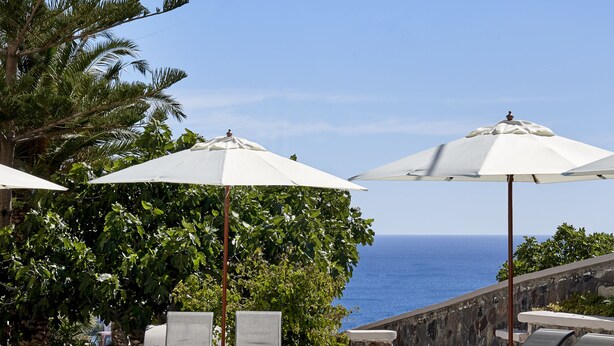A swimming pool with lounge chairs and umbrellas, overlooking a body of water. - Terra Blue Santorini (Santorini)
