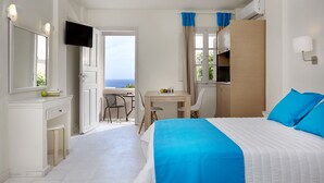 A hotel room with a bed, a desk, a chair, a TV, and a view of the sea. - Terra Blue Santorini (Santorini)
