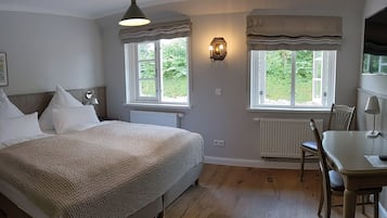 Un dormitorio con una cama grande, dos ventanas con cortinas, una mesita de noche y una silla.