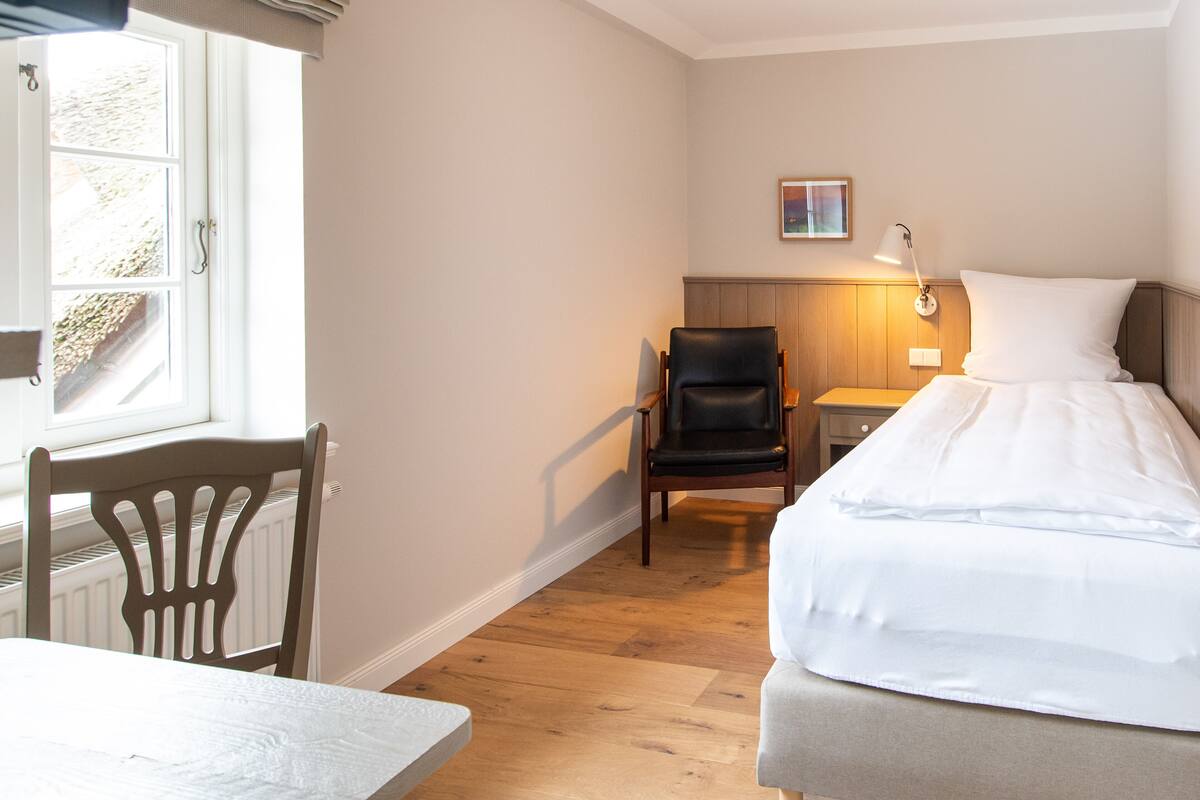 Une chambre d’hôtel avec un lit, une chaise, une table et une fenêtre.