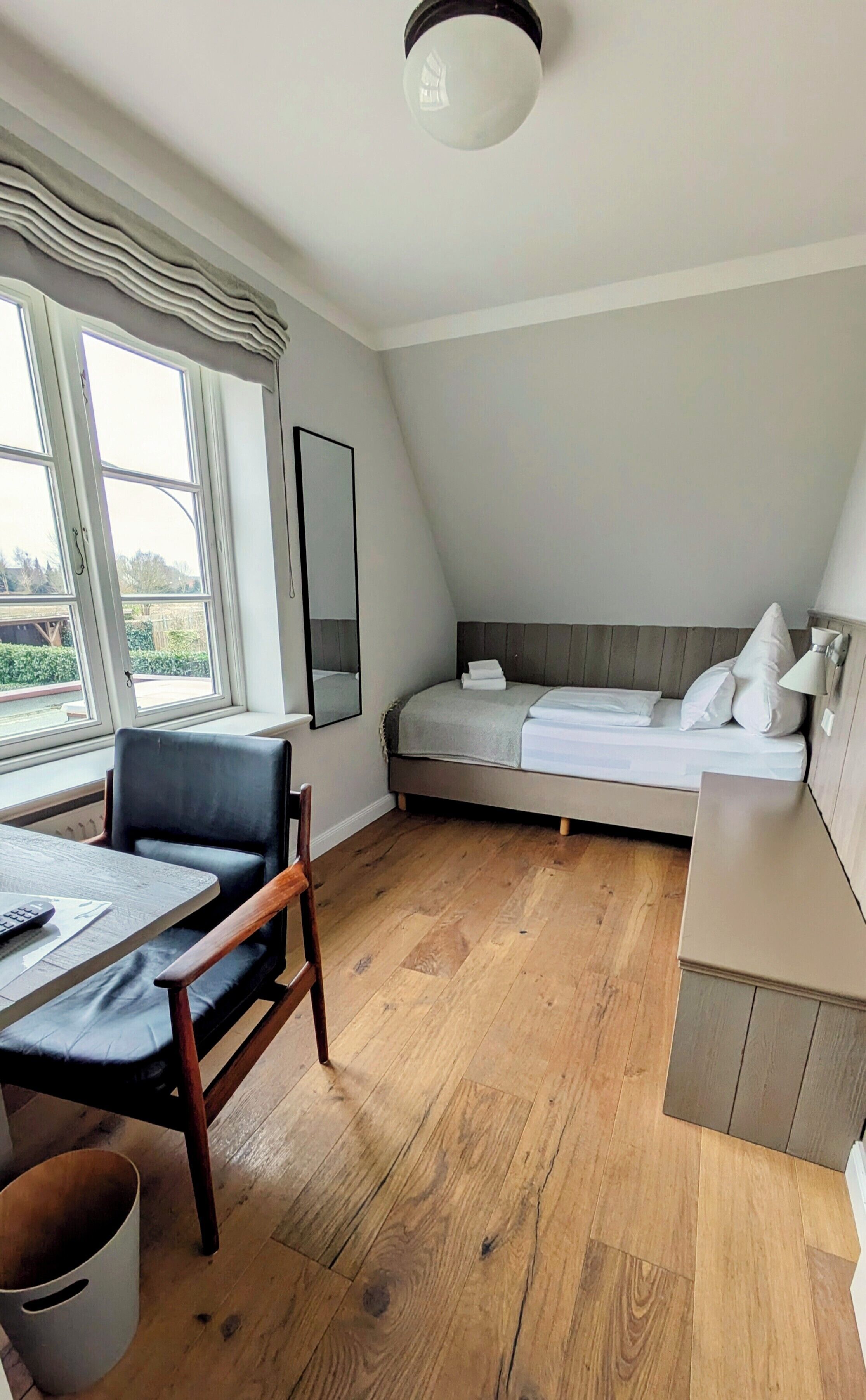 A modern bedroom with a loft bed, a desk with a chair, and a large window.