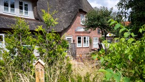 Une maison traditionnelle à toit de chaume, avec une partie en briques, entourée d’une végétation luxuriante.