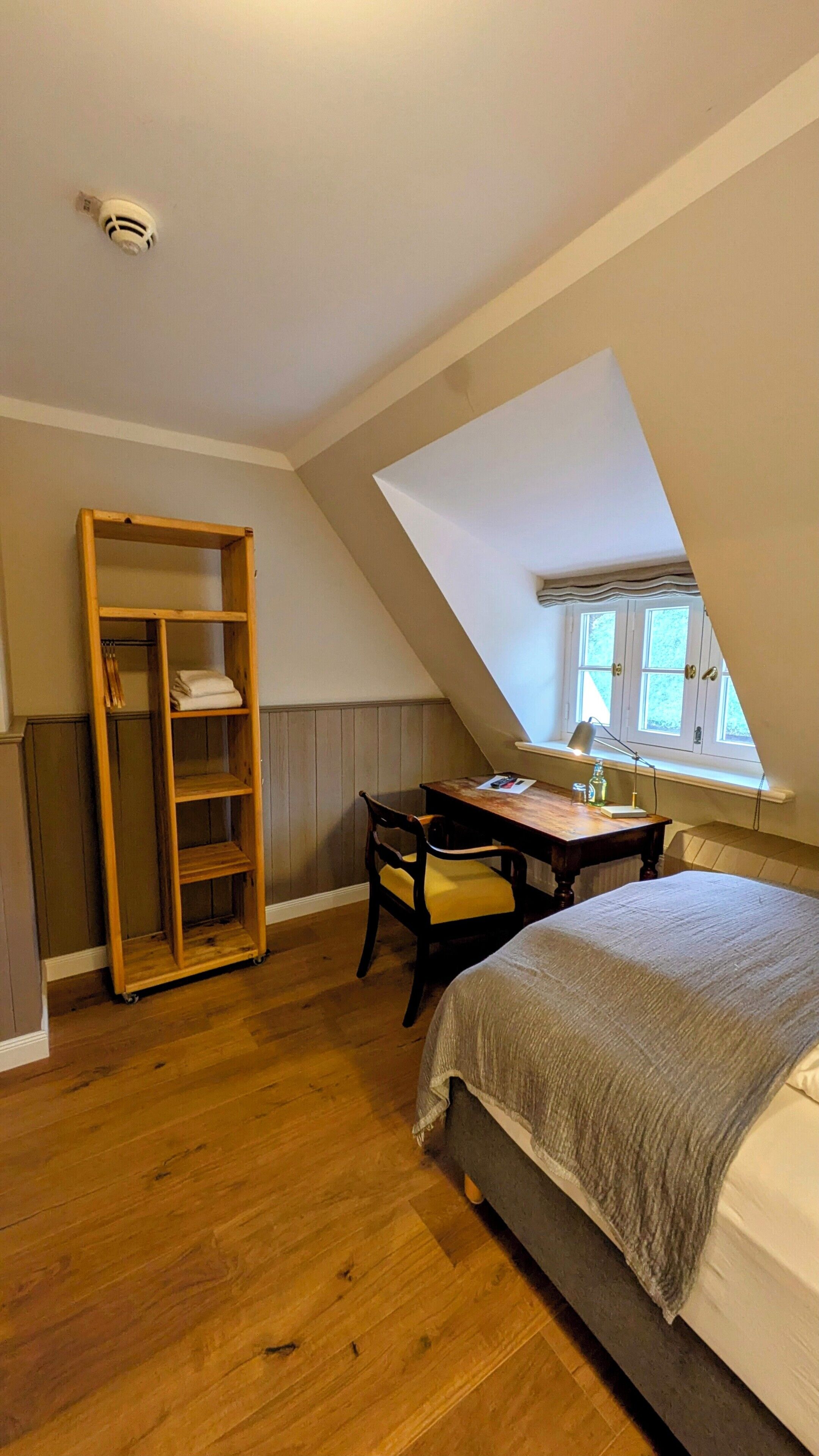 A bedroom with a loft-style ceiling, a wooden desk, a chair, a bed, and a wooden wardrobe.