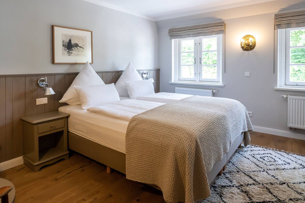 Une chambre à coucher avec un lit, une table de chevet, une lampe, une fenêtre et un tableau encadré au mur.