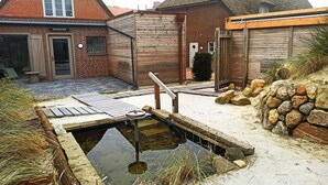 Une maison traditionnelle avec un toit de chaume, une terrasse en bois et un petit étang.