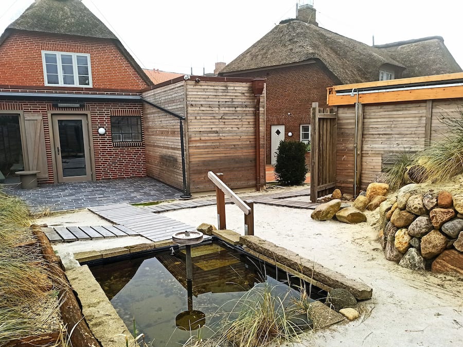 A traditional house with a thatched roof, a wooden deck, and a small pond.