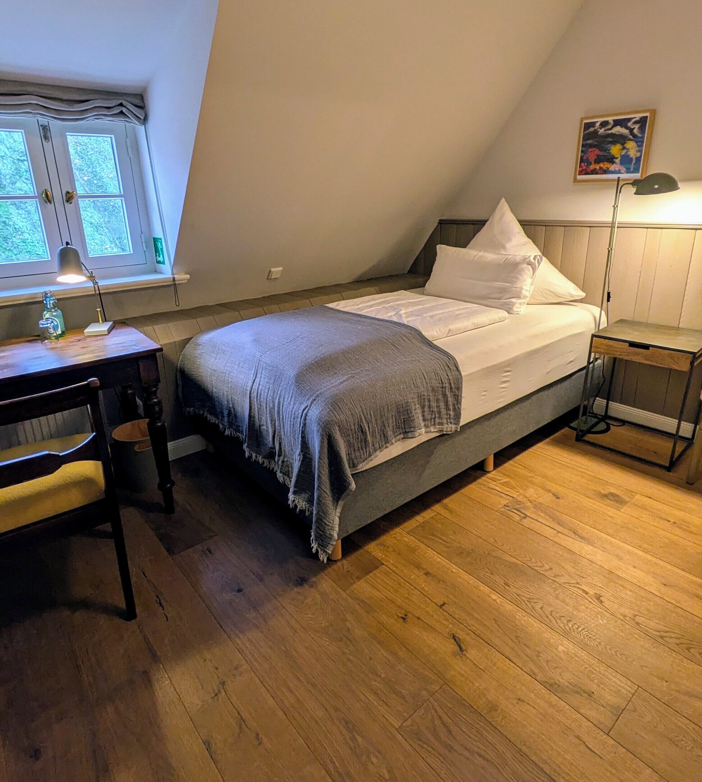 A bedroom with a bed, a desk, a chair, a lamp, and a window.