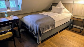 A bedroom with a bed, a desk, a chair, a lamp, and a window.