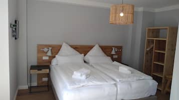 Un letto rifatto con lenzuola e asciugamani bianchi, un comodino con una lampada e una testiera in legno.