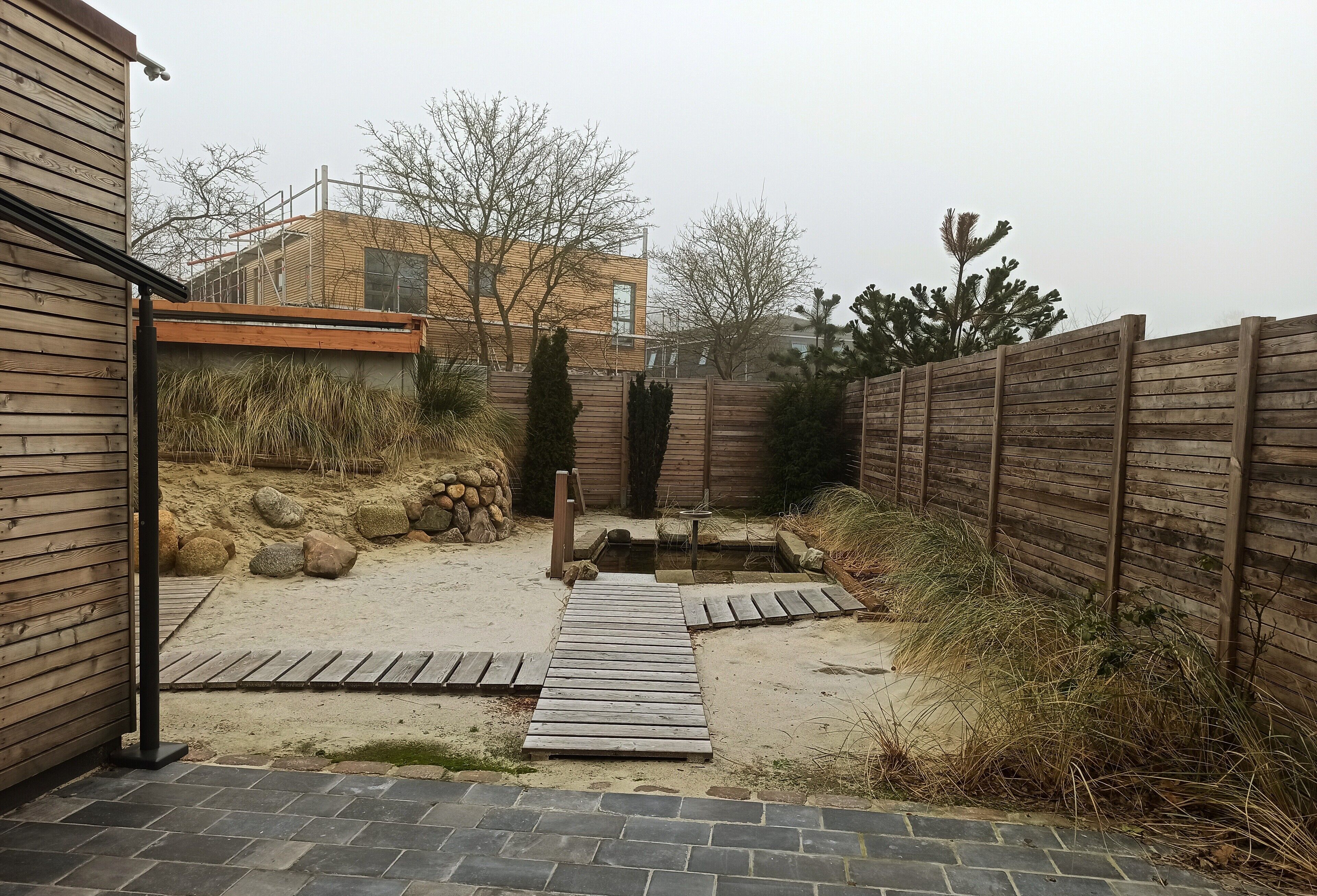 Un patio trasero con una terraza de madera, un pequeño estanque y una valla de madera.