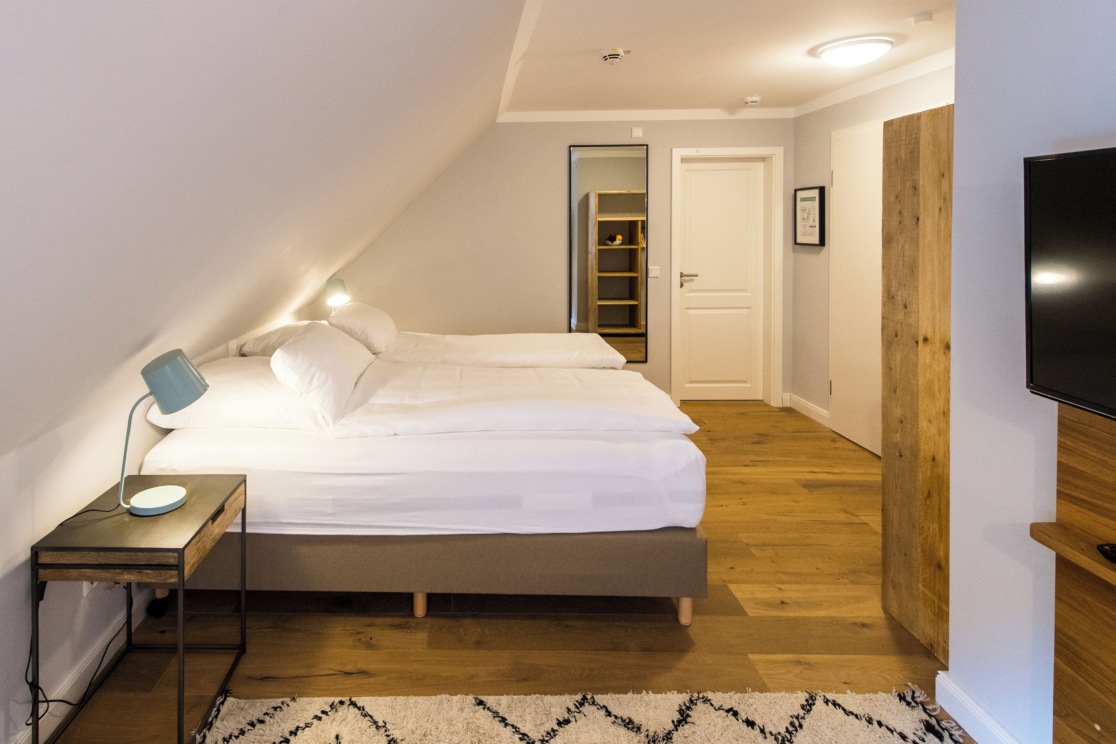 Un dormitorio con cama, mesita de noche, lámpara y televisor.
