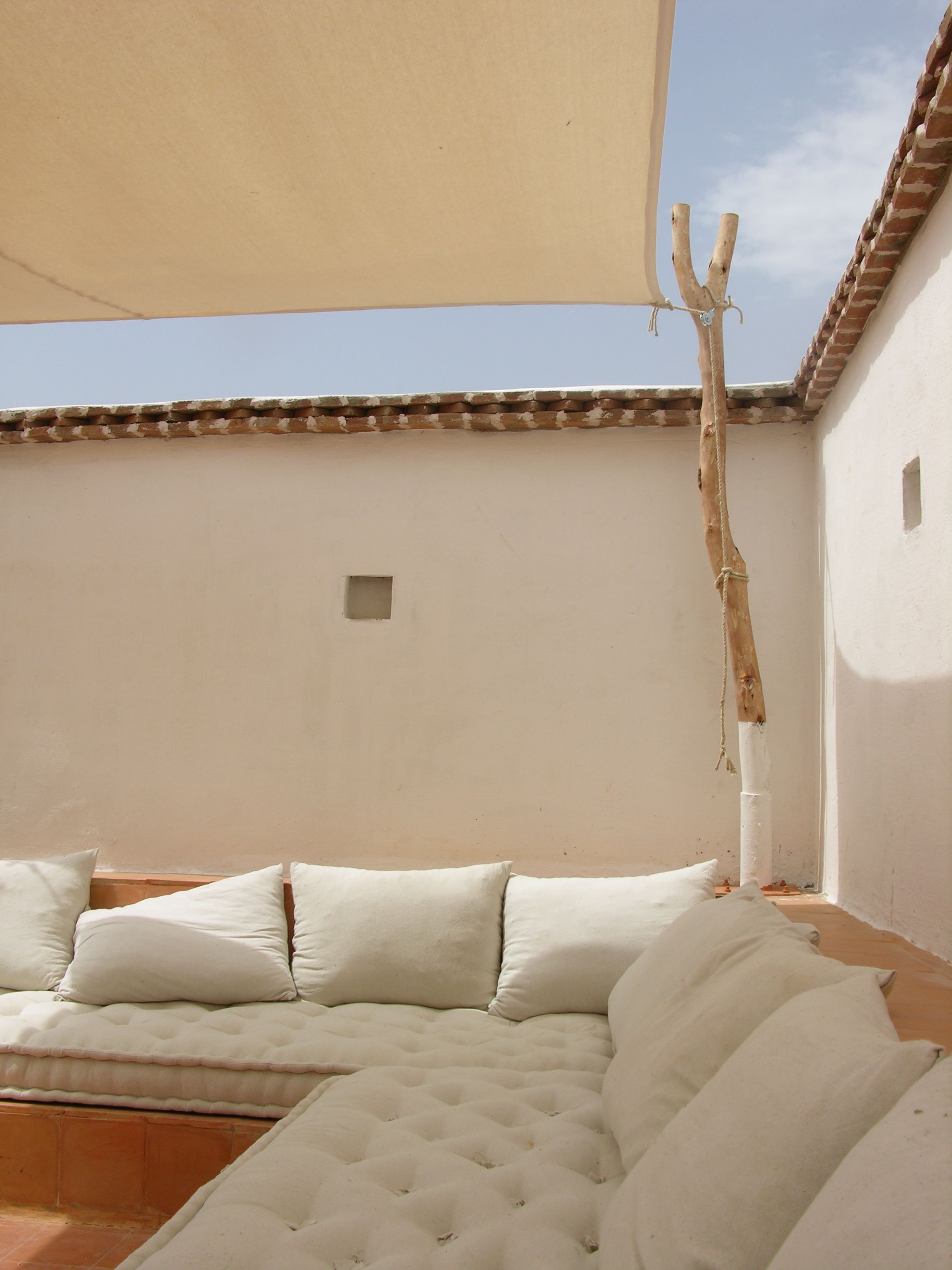 Una habitación con un sofá color beige, un ventanal pequeño y una pared blanca.