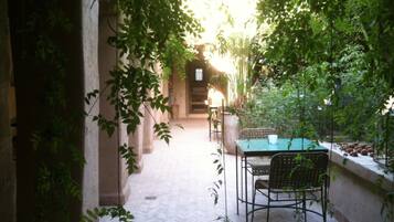 An outdoor patio with a table and chairs, surrounded by greenery and a stone wall.