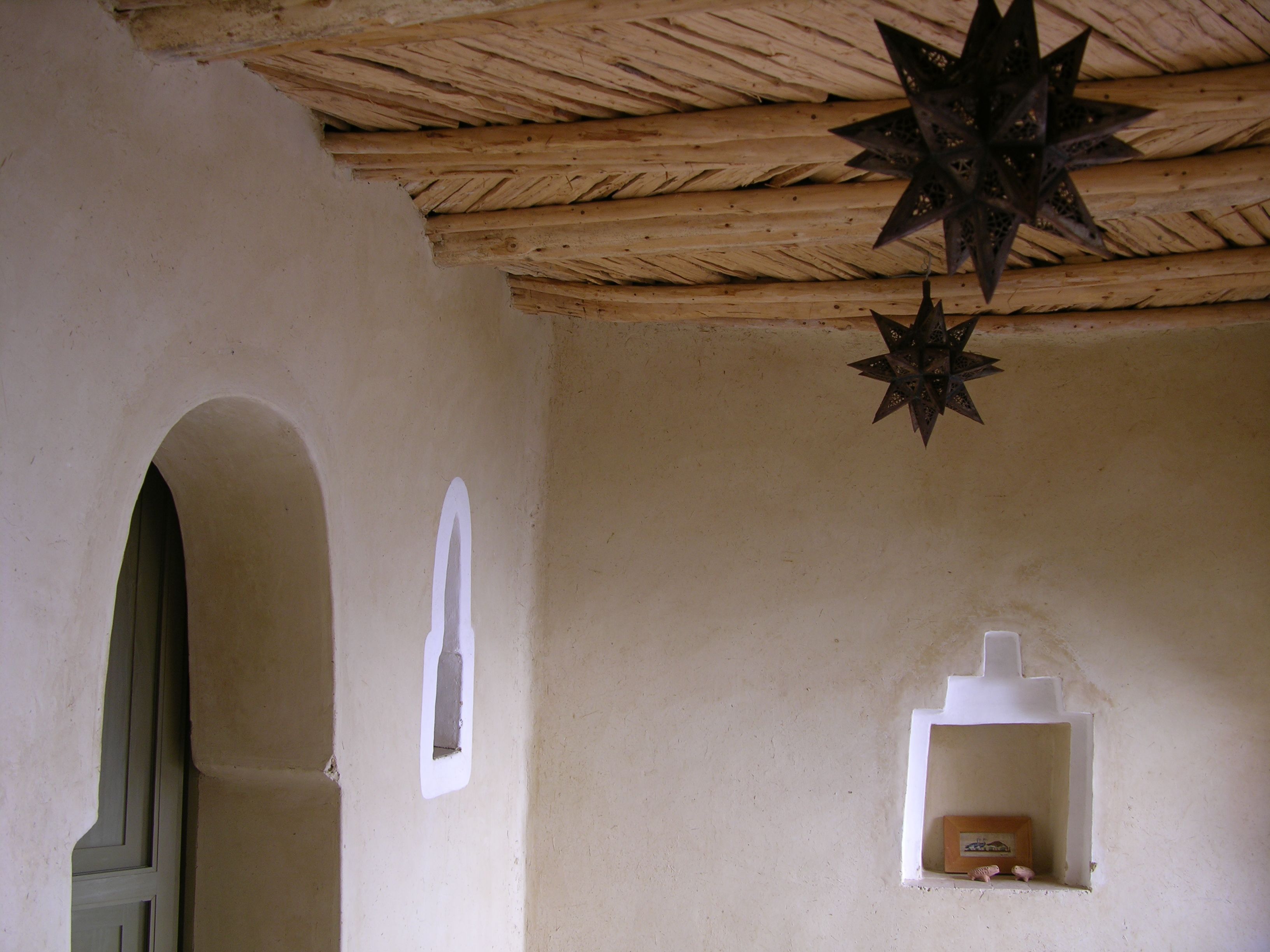 A room with a wooden ceiling, a star-shaped light fixture, a small window, and a wall-mounted shelf with a framed picture.