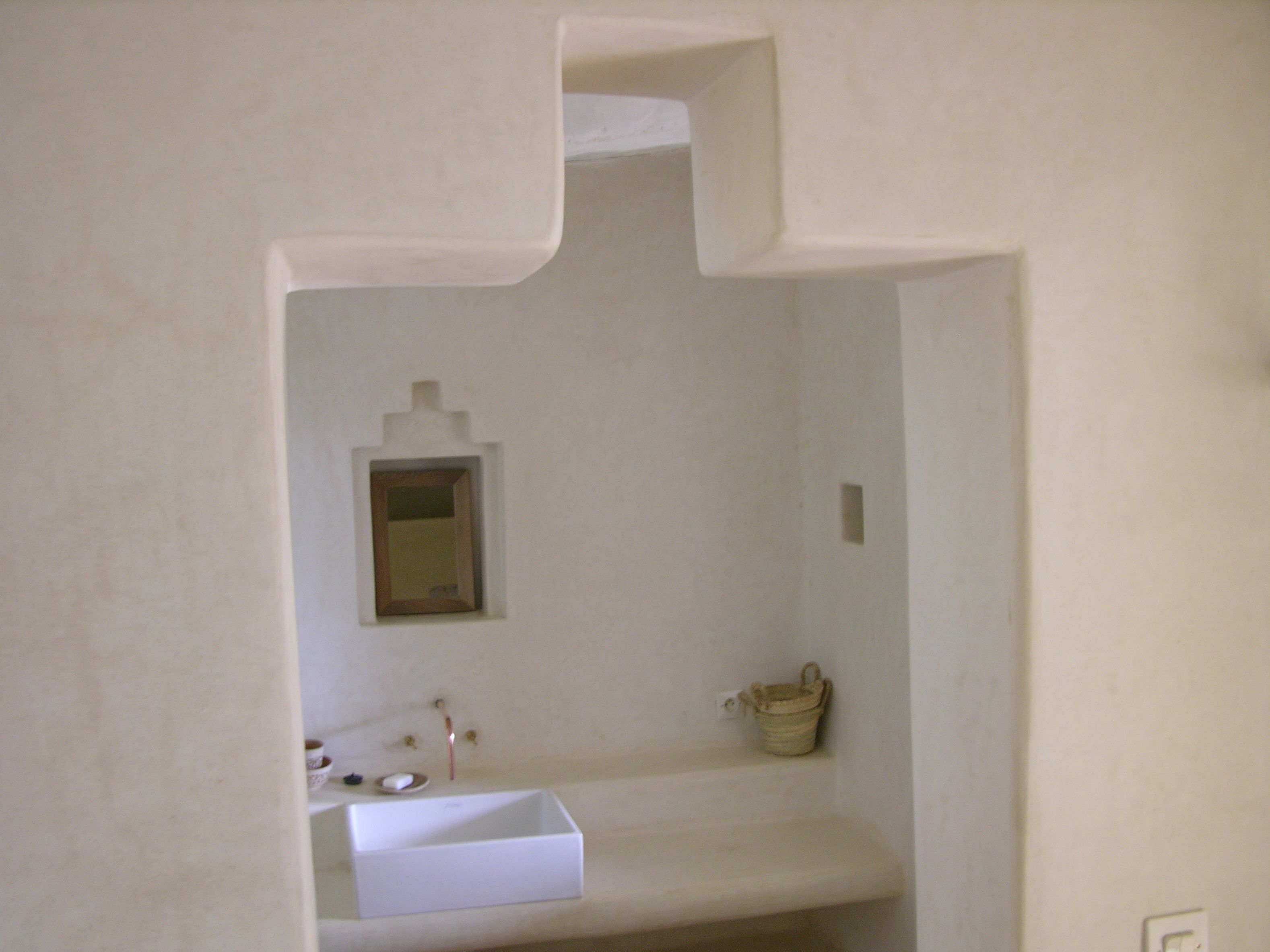 Un baño con lavamanos blanco, un espejo y un pequeño estante con artículos de aseo.