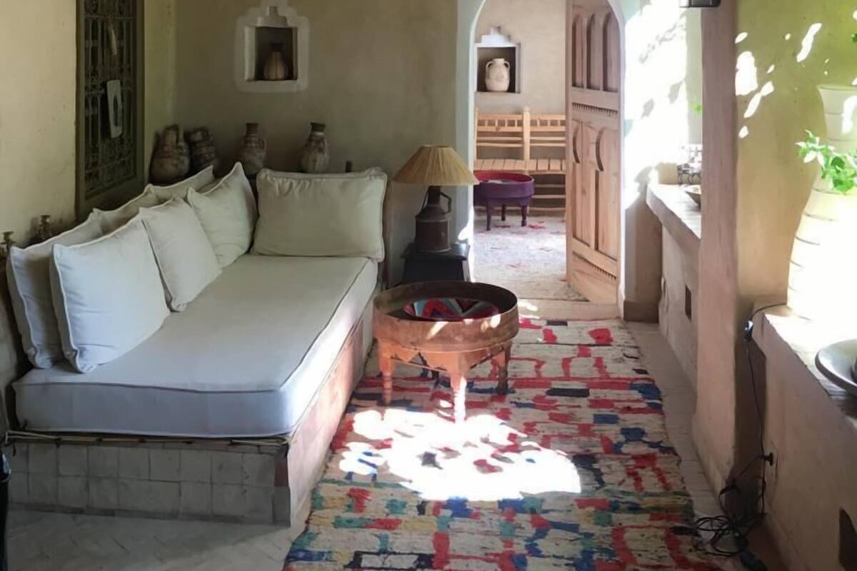 A cozy room with a wooden ceiling, a sofa, a patterned rug, and a doorway leading to another room.