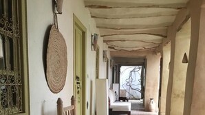 Un pasillo con una silla de madera, un tapete tejido y grandes jarrones en el suelo.