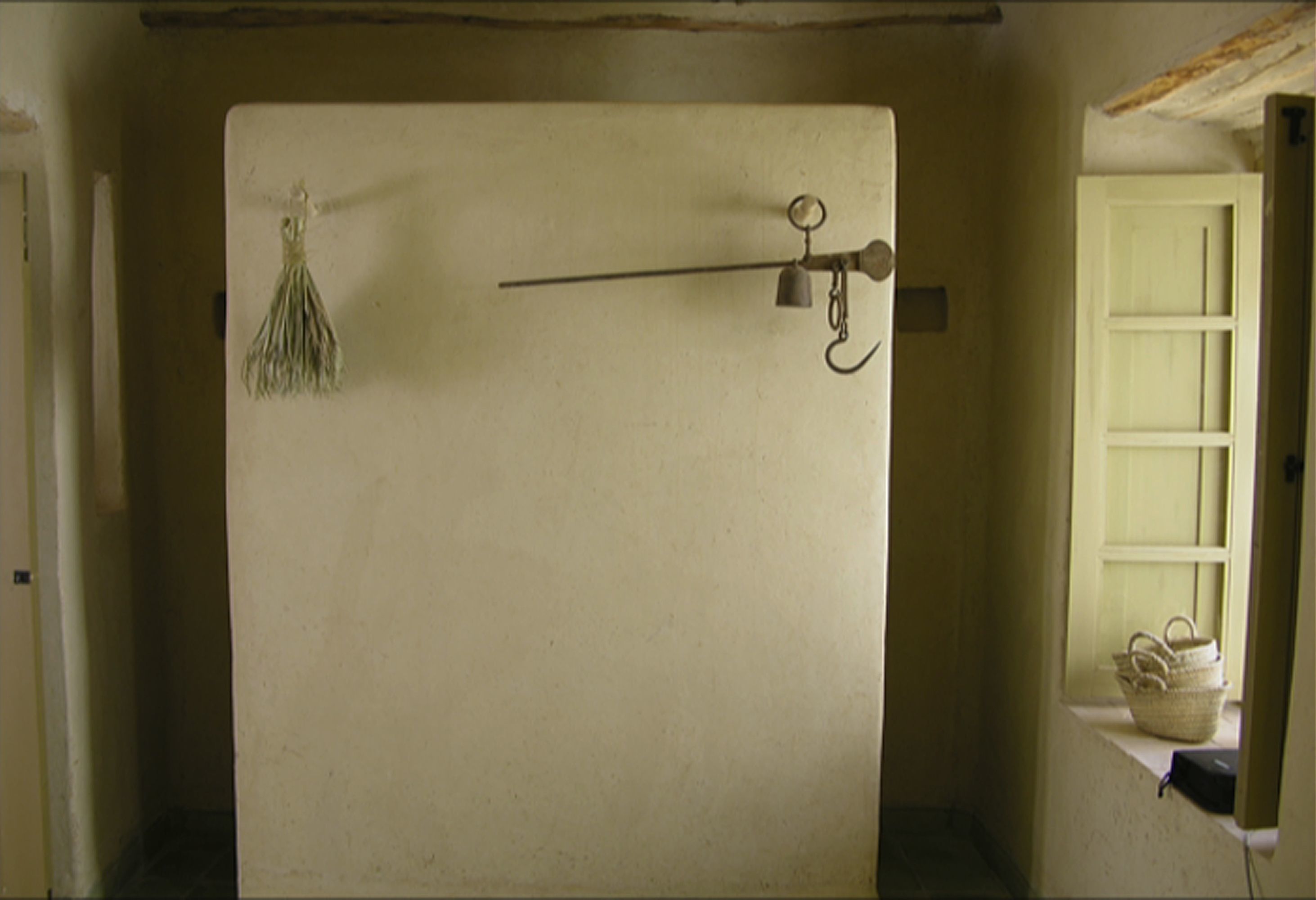 A room with a white door, a window with a basket on the sill, and a wall-mounted hook with a tassel.