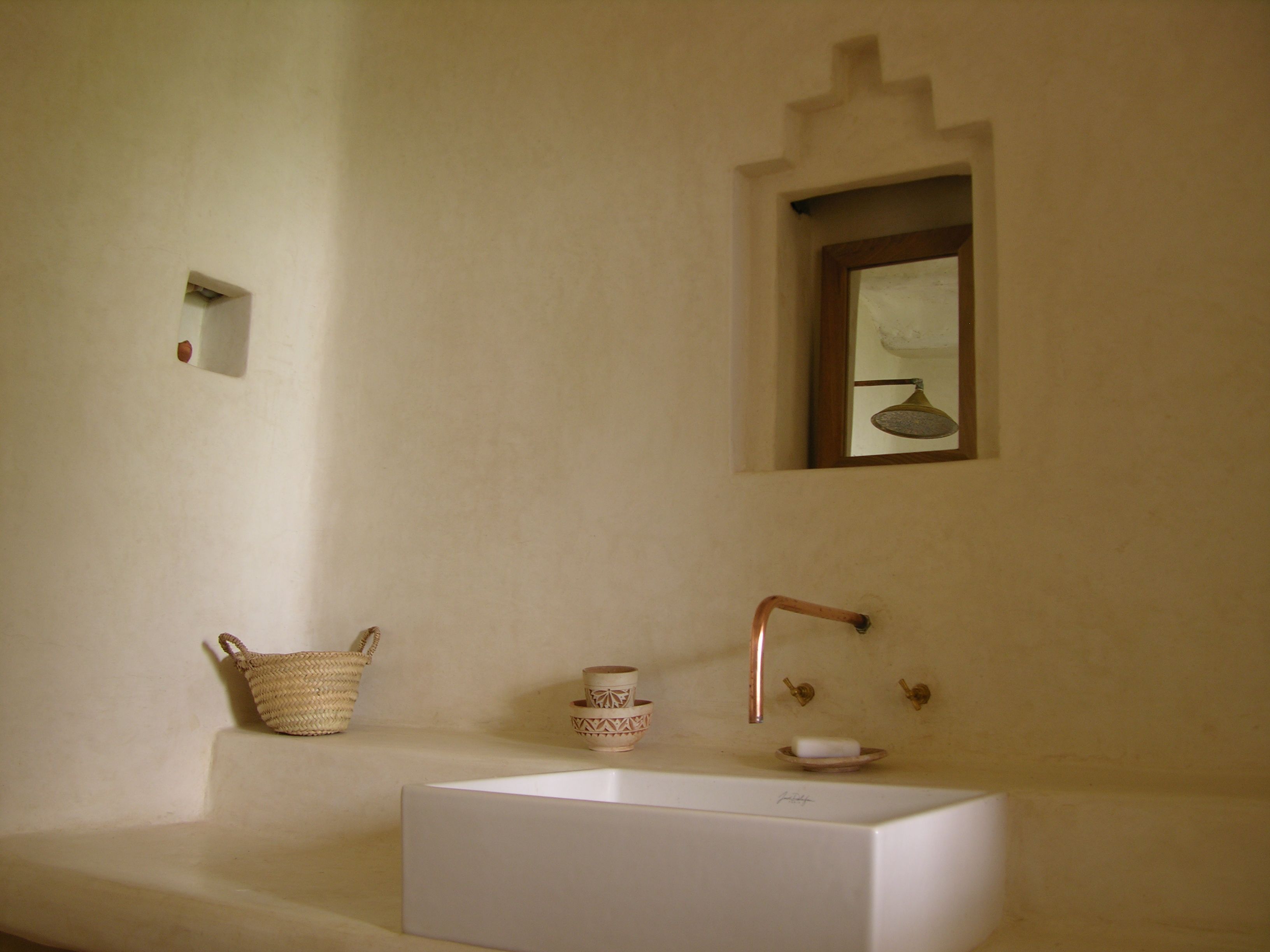 A bathroom with a white sink, a copper faucet, a small mirror, and a woven basket.