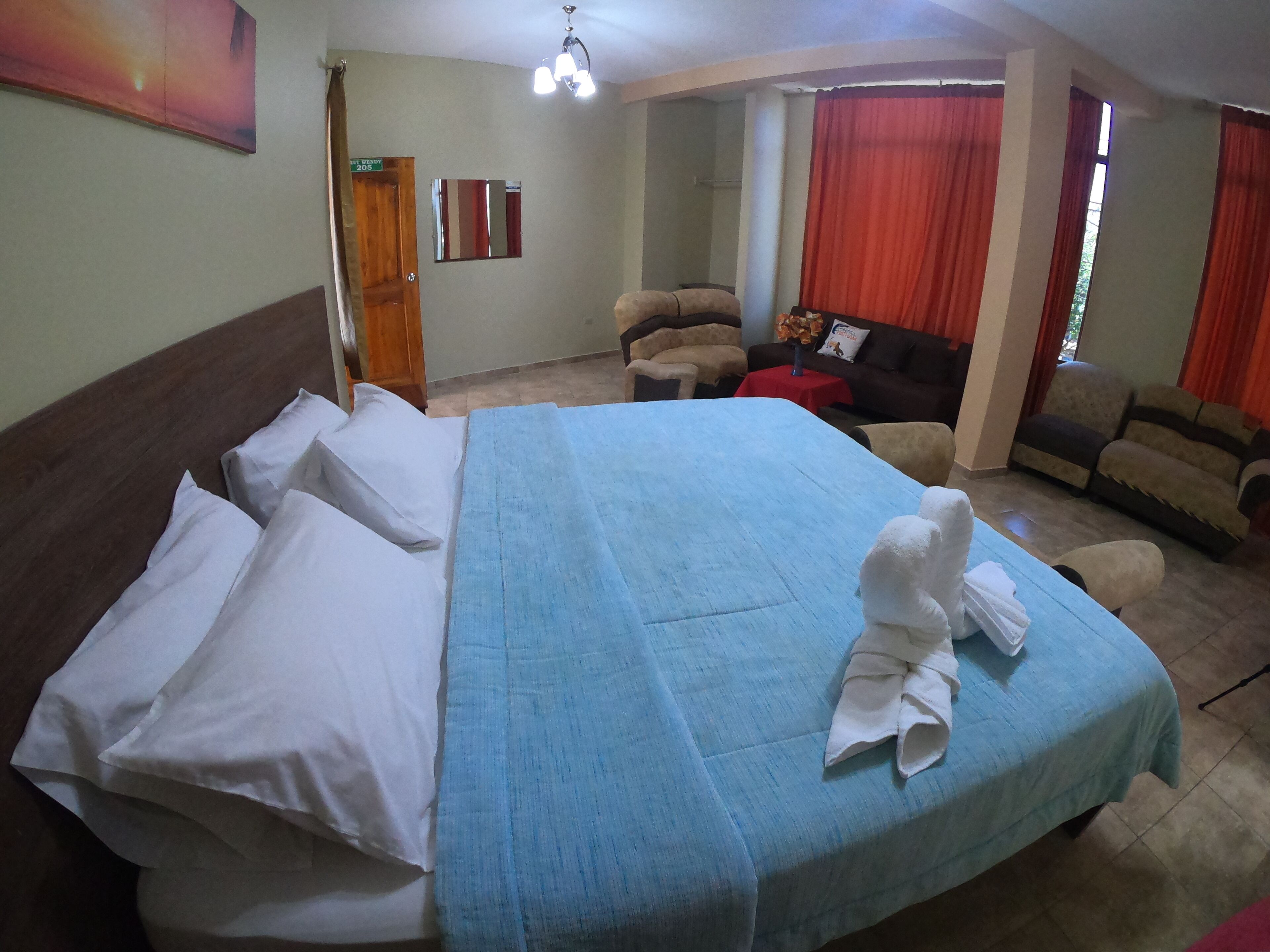 A hotel room with a bed, a sofa, a small table, and a mirror.