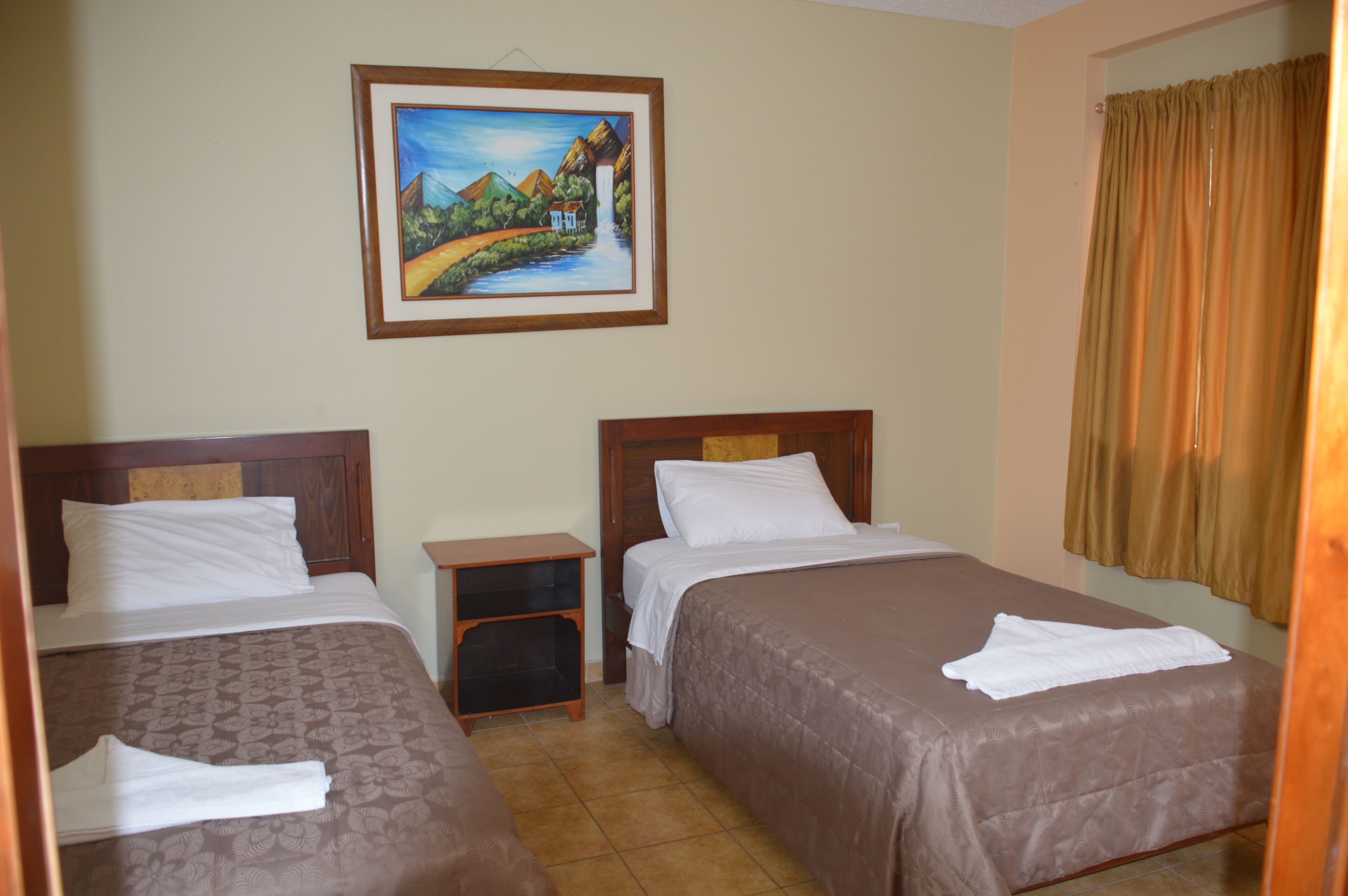 A hotel room with two beds, a nightstand, and a painting on the wall.