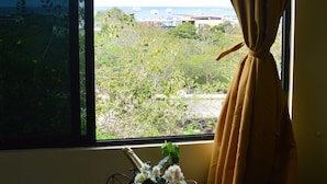 Una ventana con cortinas, un florero con flores y una copa de vino sobre una mesa.
