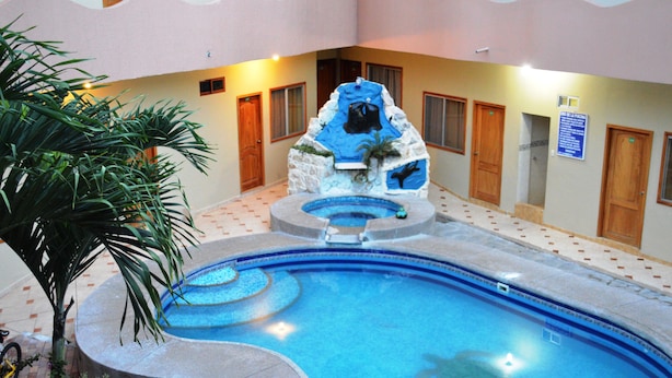 Una piscina interior con una formación rocosa como centro, rodeada de suelo de baldosas y puertas de madera.