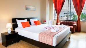 Una habitación de hotel con cama, mesita de noche, silla y ventana con cortinas.