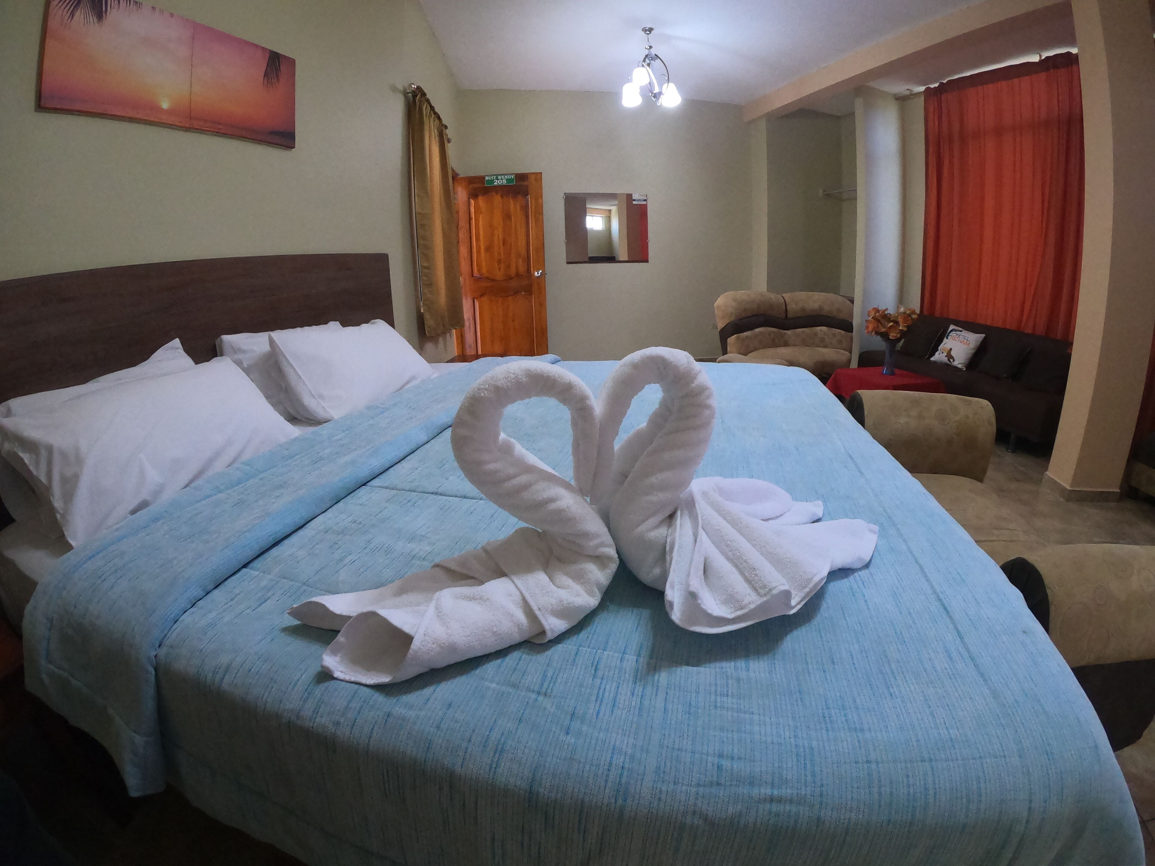 A hotel room with a bed, a blue bedspread, a towel arranged in a swan shape, a wooden door, a mirror, a red curtain, and a sofa.
