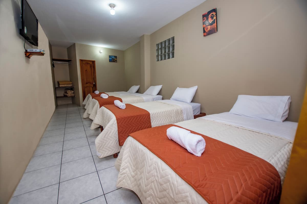 A hotel room with three beds, each with white bedding and orange throw blankets. There is a television mounted on the wall and a painting above the beds.