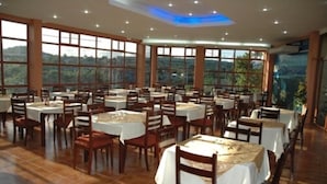 Un comedor amplio con varias mesas y sillas, ventanas grandes que ofrecen vistas al exterior, e iluminación empotrada en el techo.