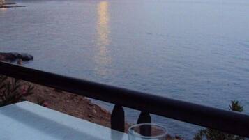 Ein Tisch mit Tasse und Glas, mit Blick auf ein ruhiges Meer und einen fernen Berg.