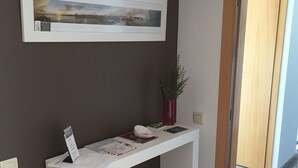 A reception desk with a framed picture above it, a vase with a plant, and a door leading to another room. - Sitges Go (Sitges)
