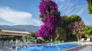 Una piscina con agua cristalina azul, rodeada de sillas reclinables blancas y una zona de estar cubierta.