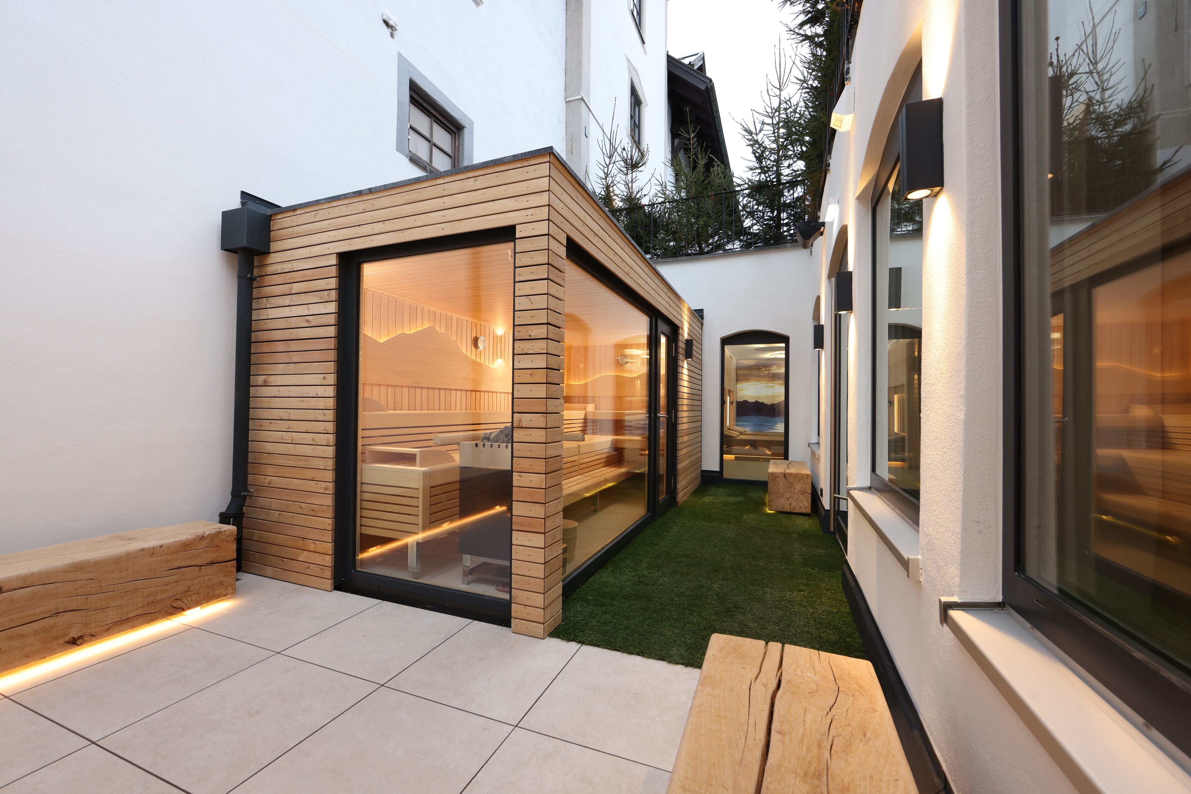 A modern house with a glass-enclosed patio, wooden deck, and a small garden area.