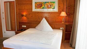 A wooden-paneled room with a bed, a bedside lamp, a telephone, and a framed painting on the wall.