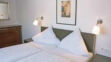 A neatly made bed with white linens, a wooden dresser, and two wall-mounted lamps.