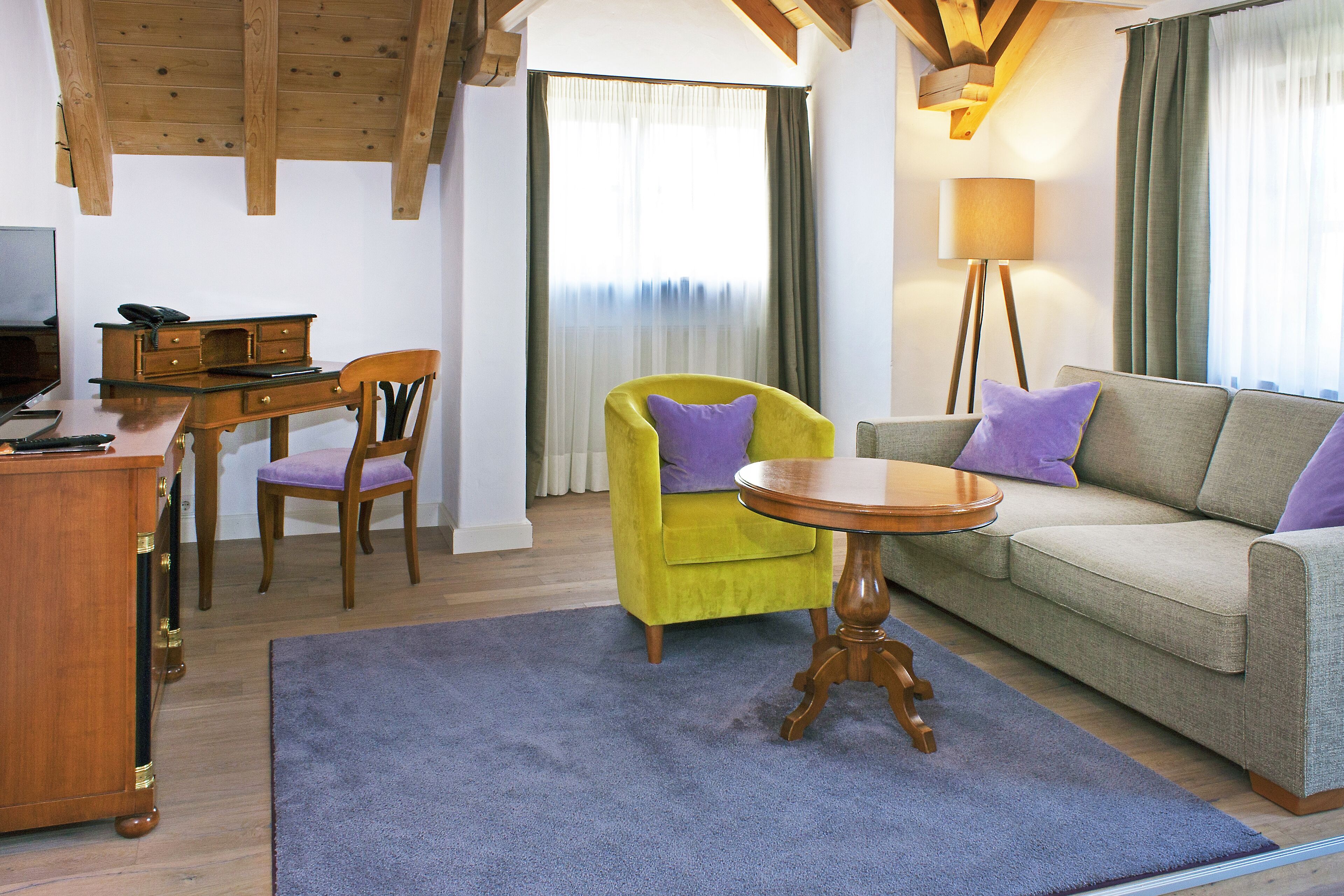 Ein Wohnzimmer mit einem Holztisch, einem gelben Sessel, einem grauen Sofa und einem runden Holztisch.