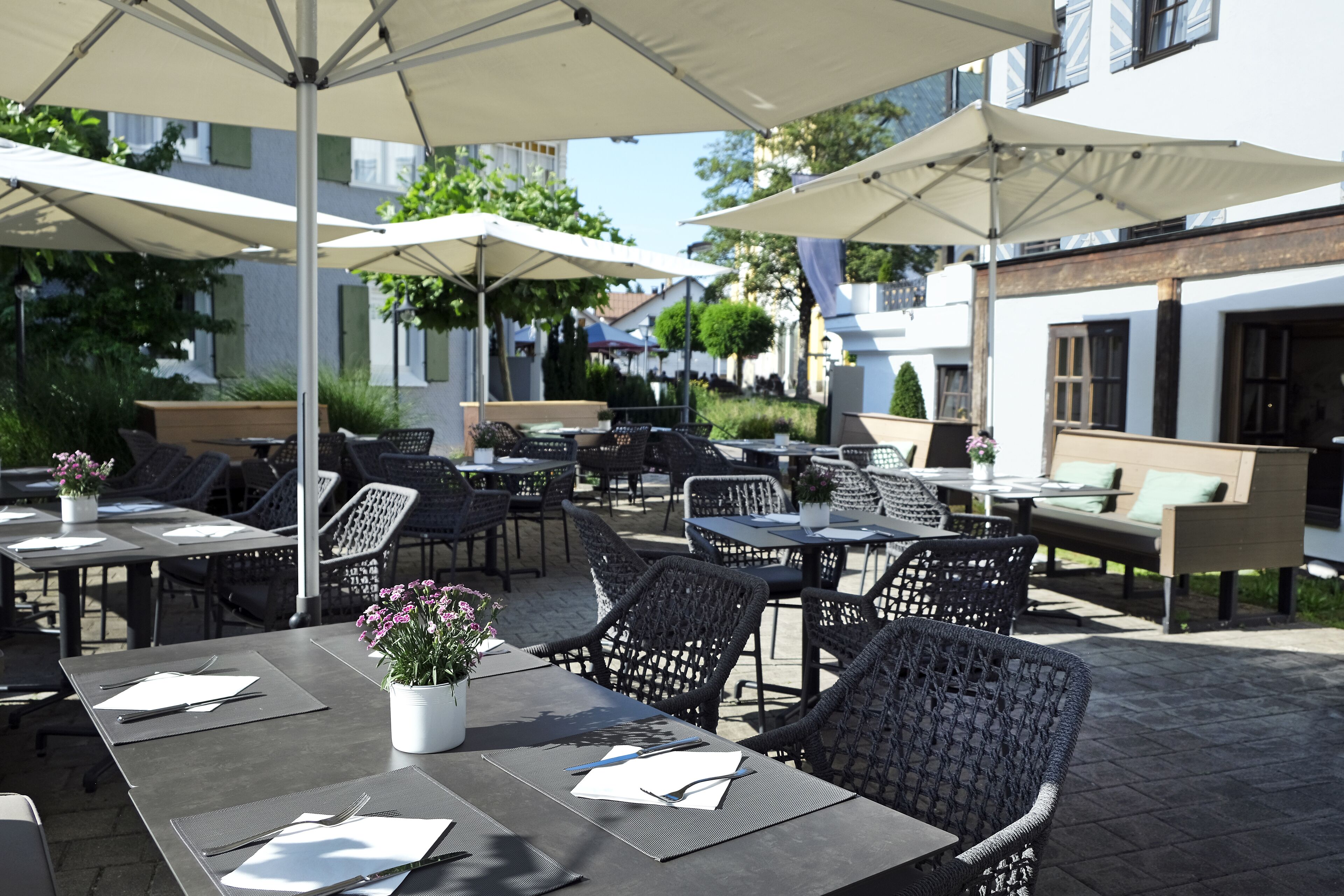 An outdoor seating area with tables and chairs, umbrellas, and potted plants.