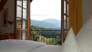 A bedroom with a large window, a bed, and a view of mountains. - Hotel Bayerischer Hof Kur & Sporthotel (Oberstaufen)