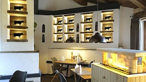 A restaurant interior with a wooden ceiling, a central dining table with chairs, and a wall-mounted shelf with cow silhouettes. - Hotel Bayerischer Hof Kur & Sporthotel (Oberstaufen)