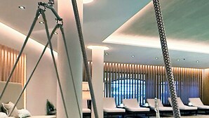 A modern indoor pool area with a swing chair, lounge chairs, and a clear view of the pool. - Hotel Bayerischer Hof Kur & Sporthotel (Oberstaufen)