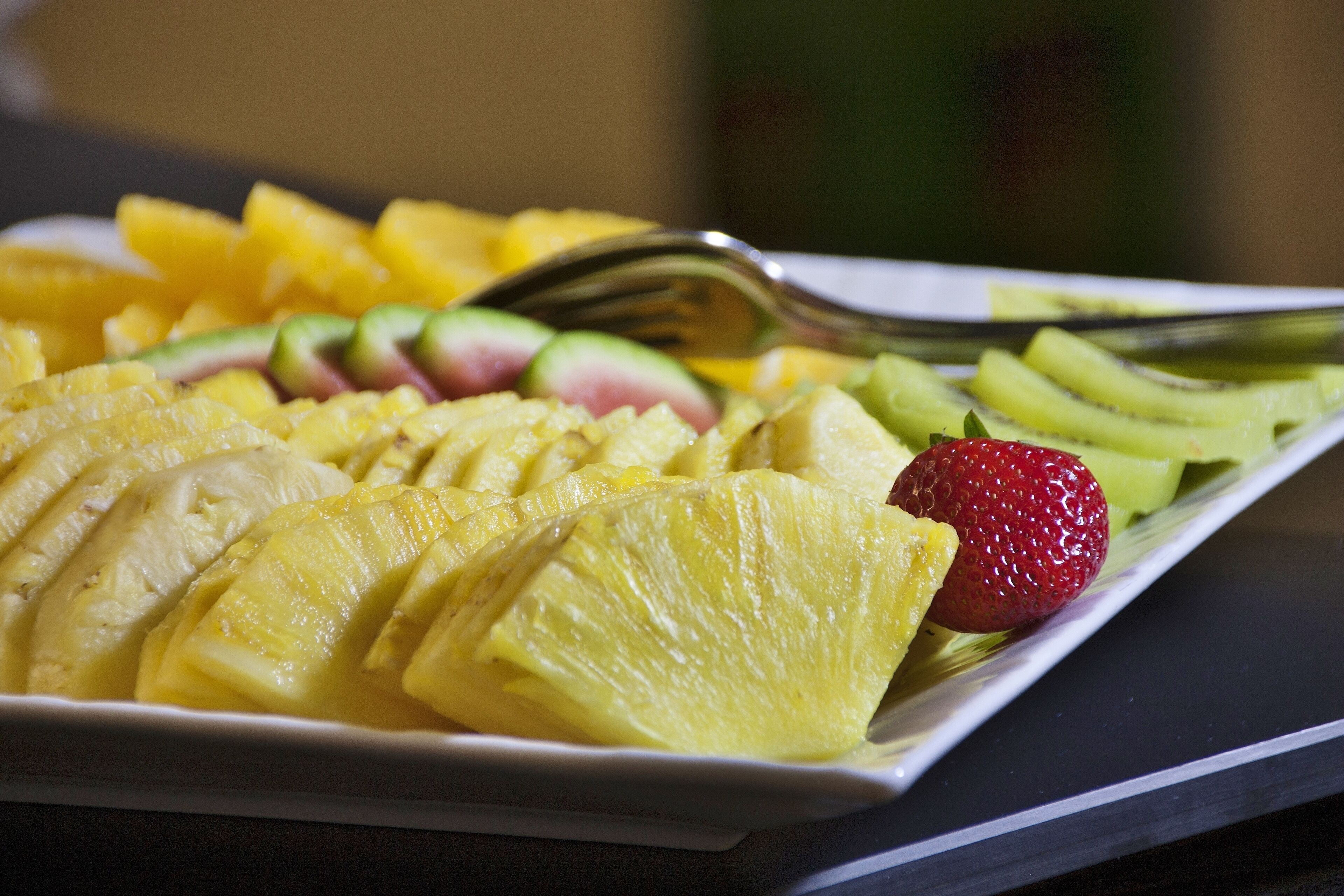 Un plato de frutas cortadas, incluyendo piña, kiwi y fresas.